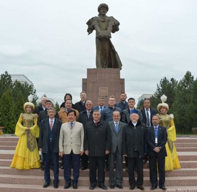 Participants in the KNU conference stand before an outdoor statue, flanked by women in traditional elegant dress.