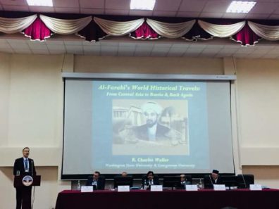 Charles Weller stands at the conference dias with a Kazakh image projected on the screen behind him..