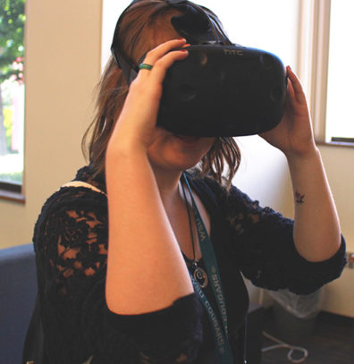 A student peers into a electronic landscape through a virtual reality headset.