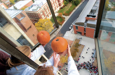 two people holding pumpkins out a 12th-story window