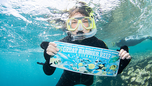 student underwater with snorkle mask and "Great Barrier Reef" sign