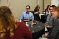 Lian Jacquez seated at a dinner table speaking with others.