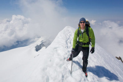 Scott pictured at the top of a snowy mountain peak, wearing cold weather hiking gear.