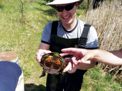 researcher holds a turtle near a pond