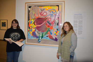Nora Loney and Linda Russo stand beside the brightly colored abstract painting Loney chose to write her poem about.