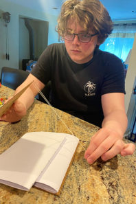 Scott Ullerich puts the first stitch into binding his book.