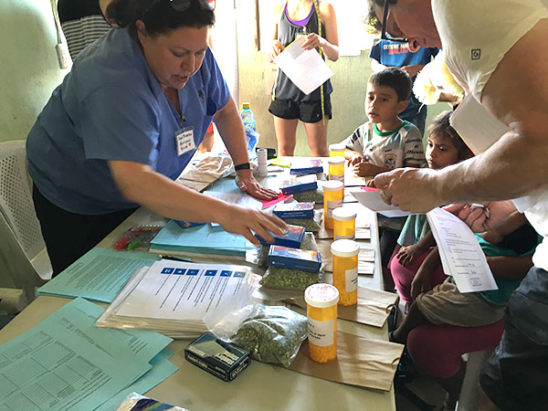 Anna Maria Rodriguez-Vivaldi talks to children and parents at a table filled with medicine bottles and literature.