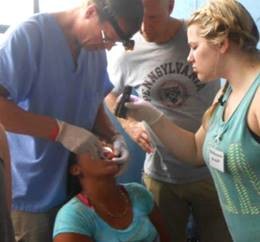 A WSU student holds a flashlight over the open mouth of child sitting in a chair while a dentist looks inside.