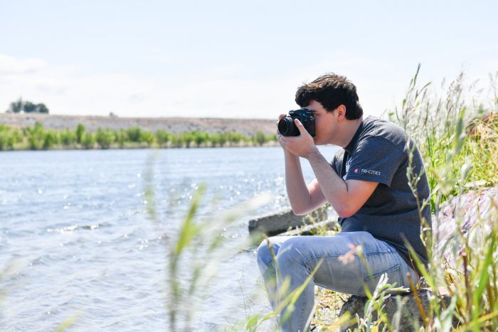 Kyle taking a photo on the bank of a river.