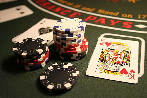Stacks of poker chips in black, red, blue, and white next to a King of Hearts playing card on a green casino table.