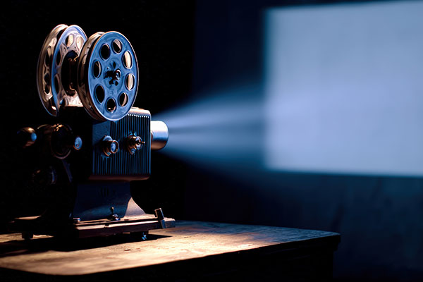 Vintage film projector on a wooden table casting a bright beam of light onto a blank screen in a dark room.