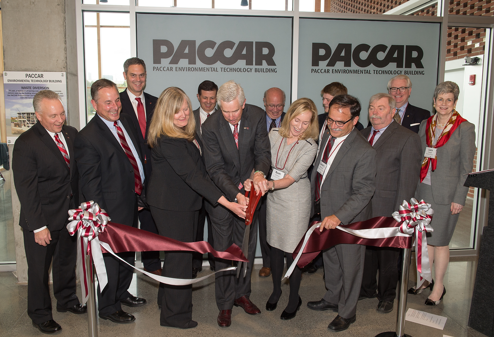 Group of people in suits cuts a ceremonial ribbon with giant scissors.
