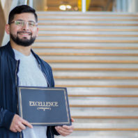 Yoni Rodriguez standing on stairs holding a certificate of excellence.
