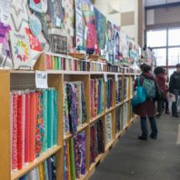 Shoppers browse long row of shelves full of colorful fabrics.