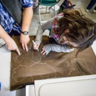 Shot from above, a young girl traces a pattern onto faux fur