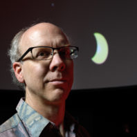 Astronomy instructor Michael L. Allen poses in the WSU Planetarium Monday, July 31, 2017, with a depiction of the moon crossing in front of the sun.