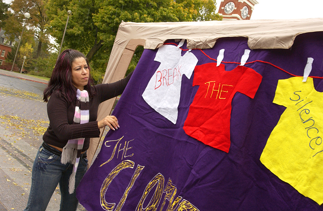 Image of a student hanging a sign that says "Break the Silence!" at a Clothesline Project demonstration.