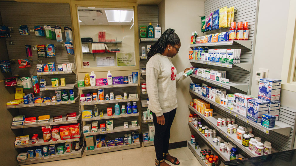 student in pharmacy looking at item from over the counter product shelves