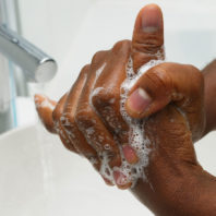 clasped hands under running water in a sink with soap suds