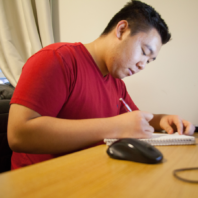 Student in dorm at desk writing in notebook.