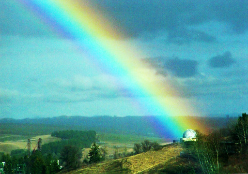 A rainbow that is in the background of a observatory on a hill