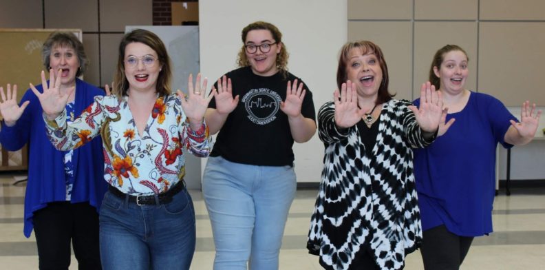 a photo of five women in a row with their arms extended forward and hands up