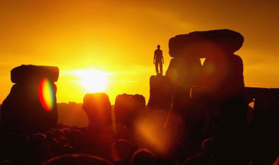 A photo of the sunset at Stonehenge with a human on one of the stones