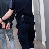 Prison guard escort inmate throught corridor in jail corridor for booking after arrest.
