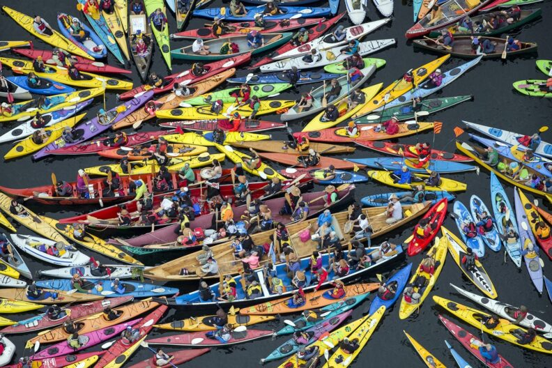 The image emphasizes the power in numbers and also the colorful and compelling nature of kayaktivism.