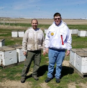 Riley Reed with Dr Hopkins in the beekeeping field, some bees flying around