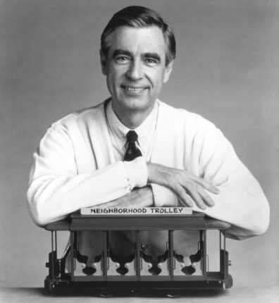 A photograph of Mr. Rogers with his arms crossed on top of Trolley.
