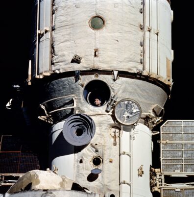A photo of a space capsule with a cosmonaut's face visible through a round window
