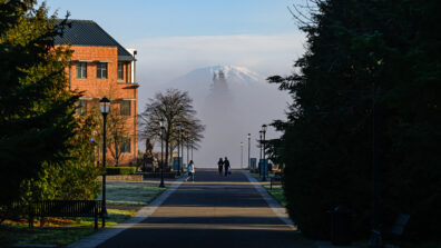Students walk down a pathway at WSU Vancouver with a red brick academic building visible to the left and St Helens shown at the end of the path