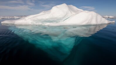 An iceberg floating in the ocean with the white snowy top and blue underside both visible
