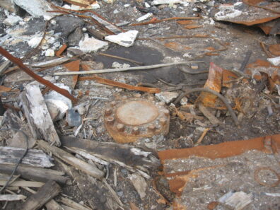 The metal-capped borehole with visible rivets sits in rubble