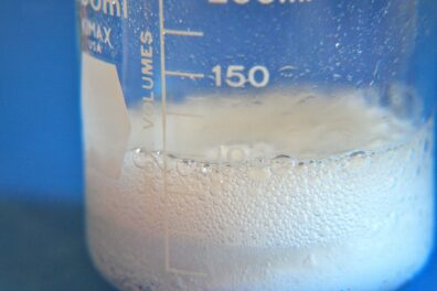 A glass beaker containing a white liquid bubbles