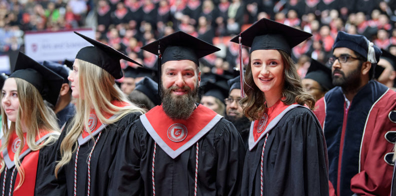 Dan Richer and Kelley Sindelar wearing graduation caps and gowns at a WSU Commencement.