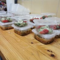 plastic bins of food with lettuce and tomato on lids