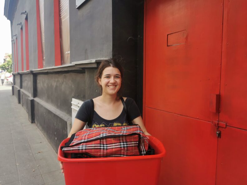 young woman smiling at camera holding a red bin with a red plaid bag inside