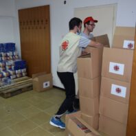 two young men working at stacked boxes inside a big room