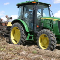 A picture of a 5100 M John Deere tractor pulling a potato digger.