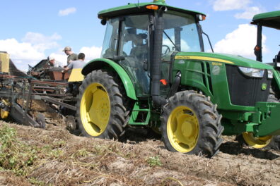 A picture of a 5100 M John Deere tractor pulling a potato digger.