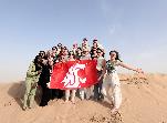 group of students standing on sand holding a WSU flag