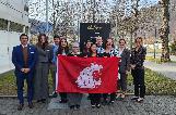 group of students standing on a grassy, treed area between buildings holding a WSU flag