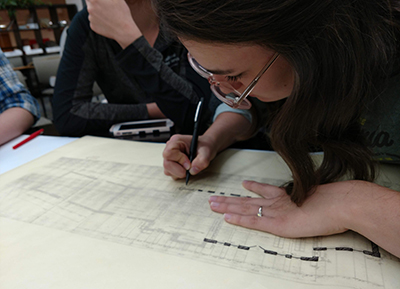 Student with pencil in hand adding detail to an architectural drawing.