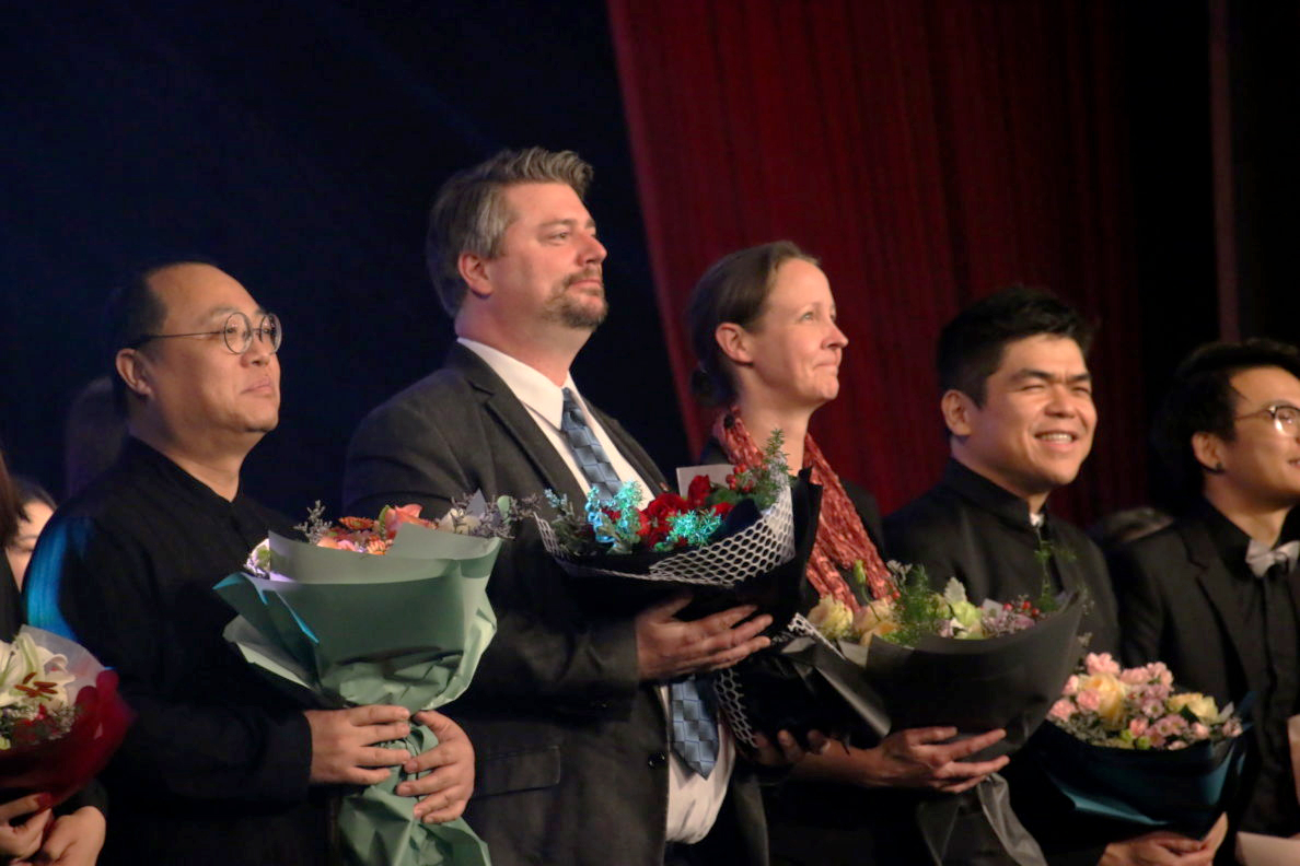 Pham, Boden and Luethi holding flowers with several Guangzhou University Symphony Orchestra members.