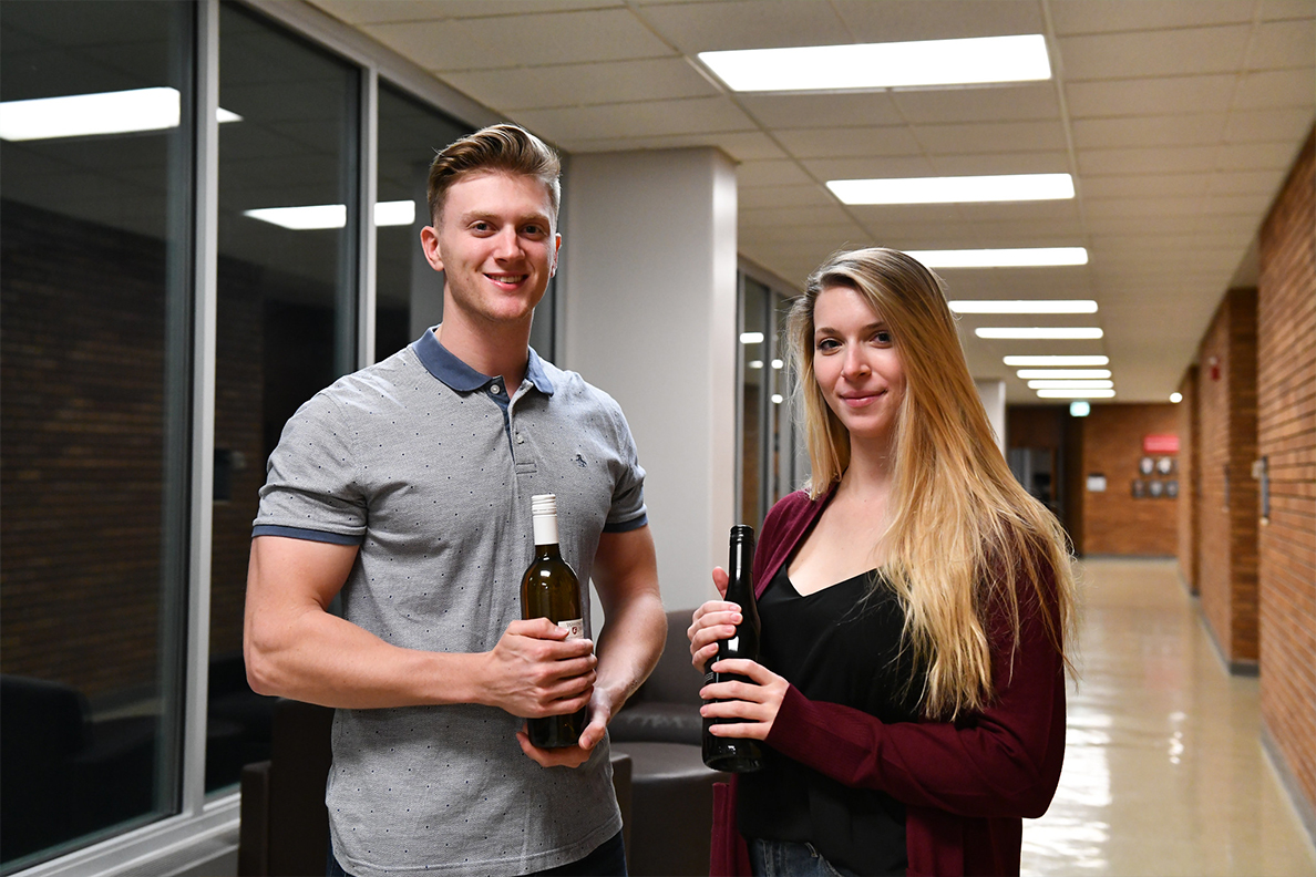 Two students poise for a picture while holding bottles of wine.