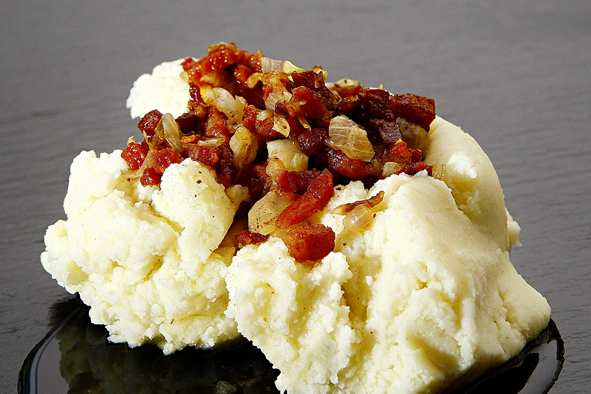A closeup of mashed potatoes with bacon toppings.