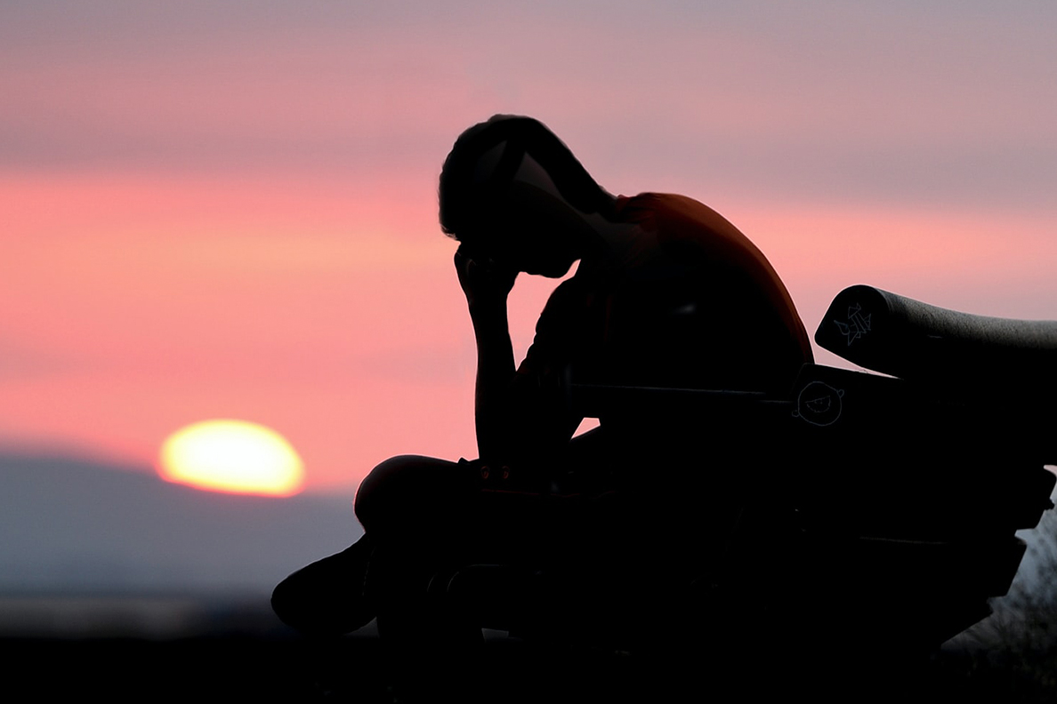 Silhouette of young man on bench with his head on his hand.