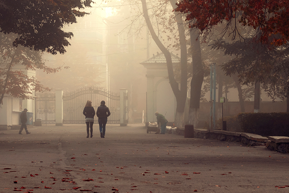 People walk along a smoky street.